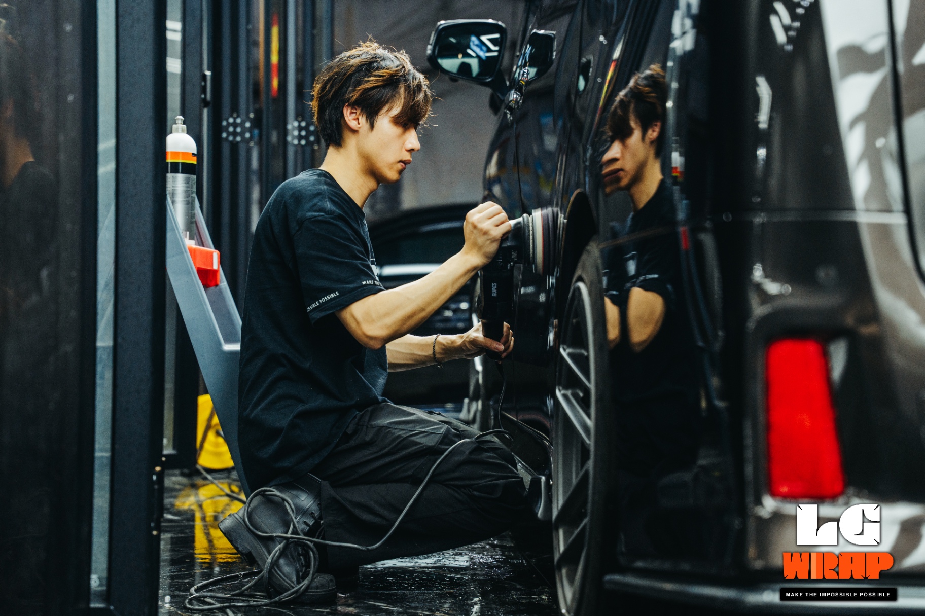 Technician crouching to meticulously polish the rear wheel arch of a dark MPV