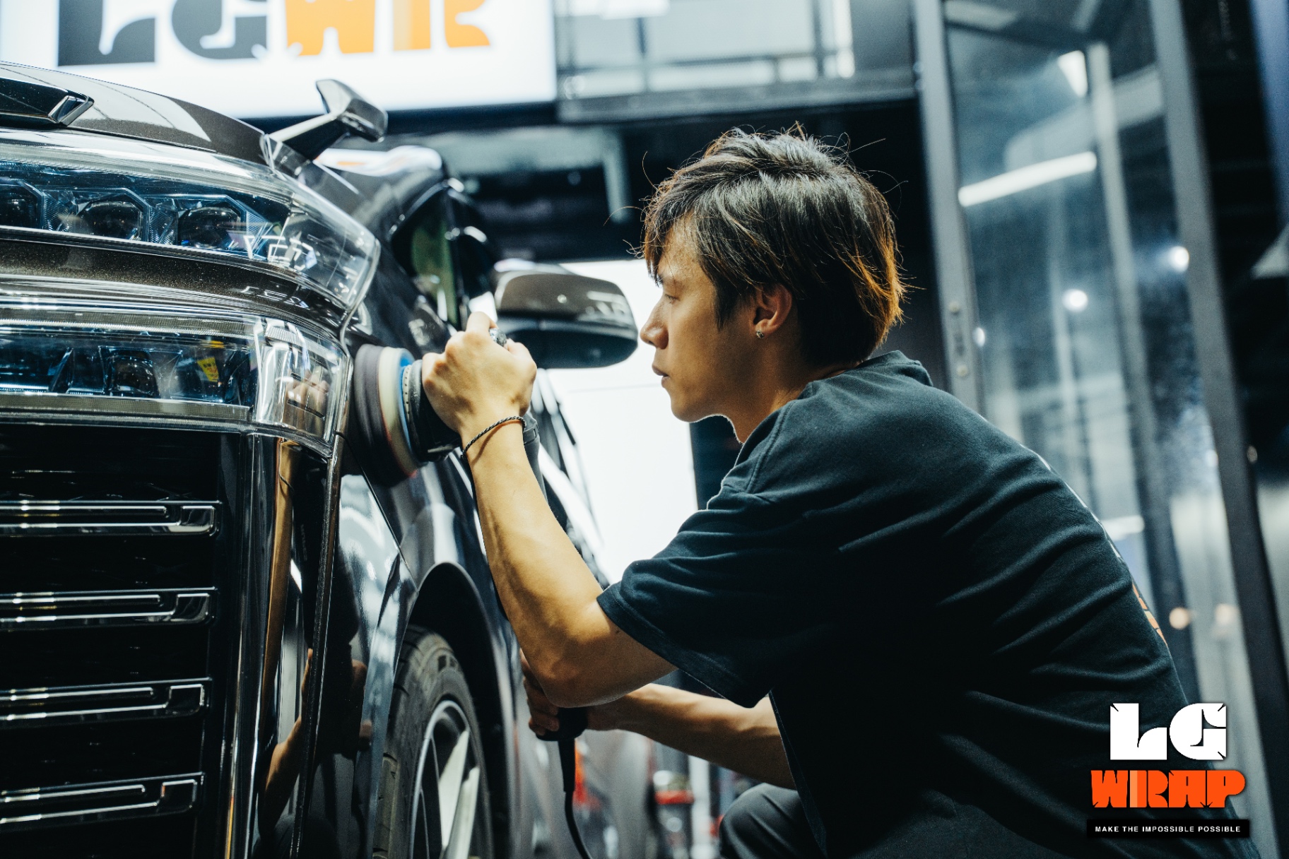 Technician polishing the front fender of a dark MPV