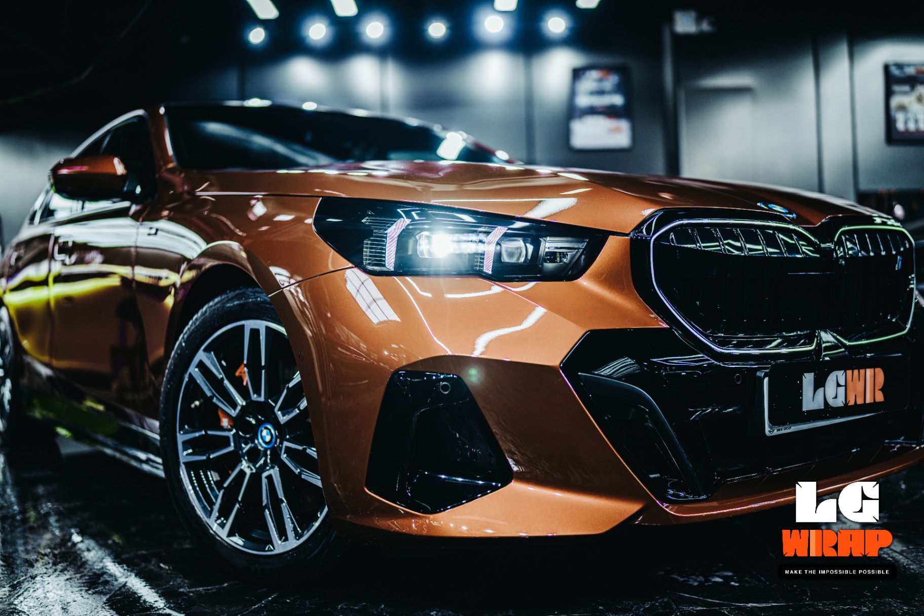 Front-end close-up of an orange BMW i5 M Sport under showroom lights, showcasing the deep reflection of Colour PPF